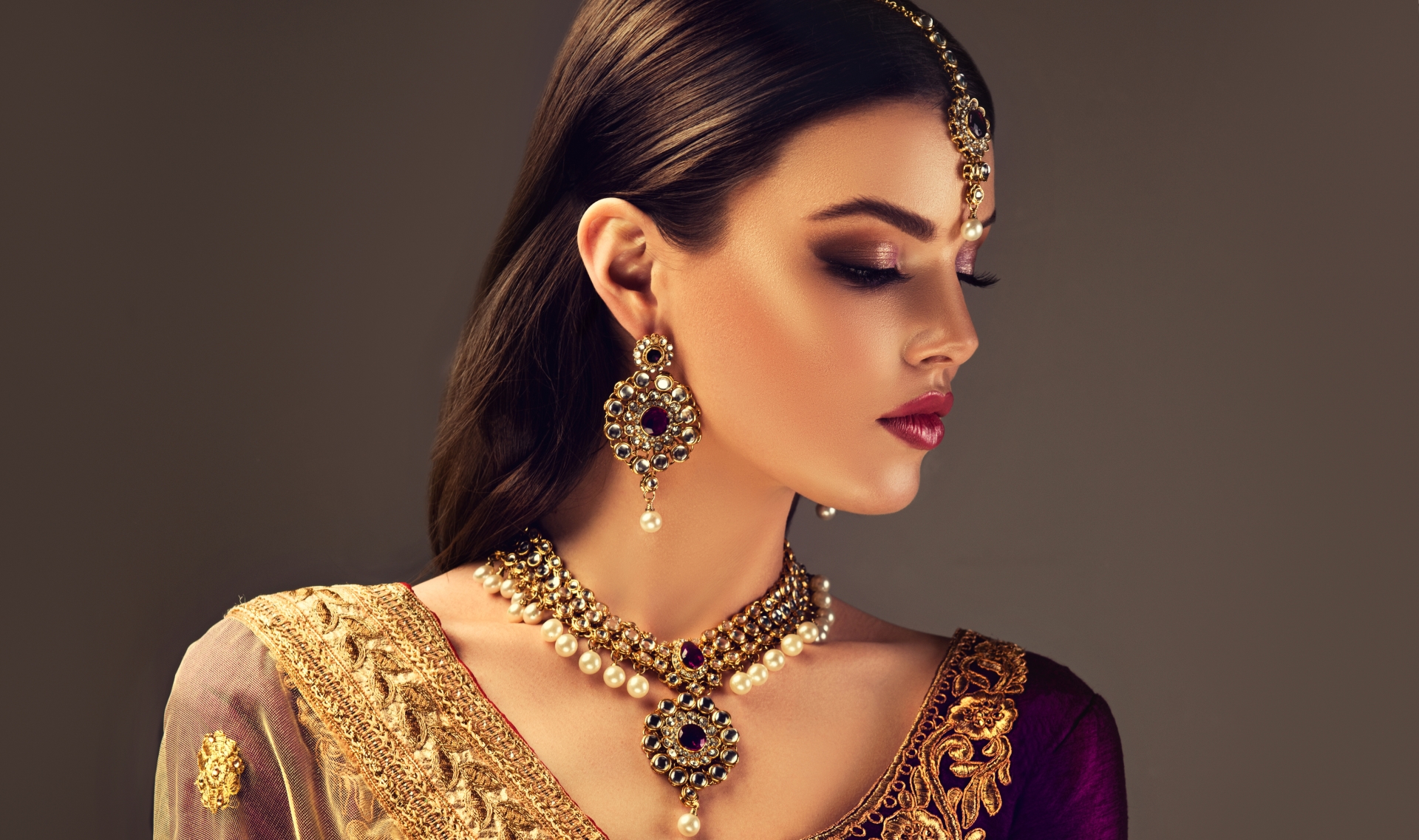 Young gorgeous black haired woman in a splendid makeup, dressed in a traditional indian blouse and national jewellery set made from stones and pearls,consisting of big bright earrings, necklace and head adornment (tikka). Indian beauty.